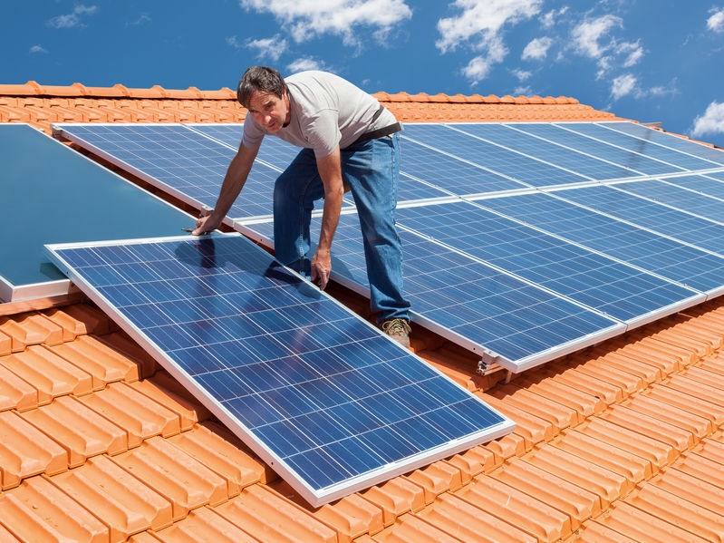 Man installing alternative energy photovoltaic solar panels on roof