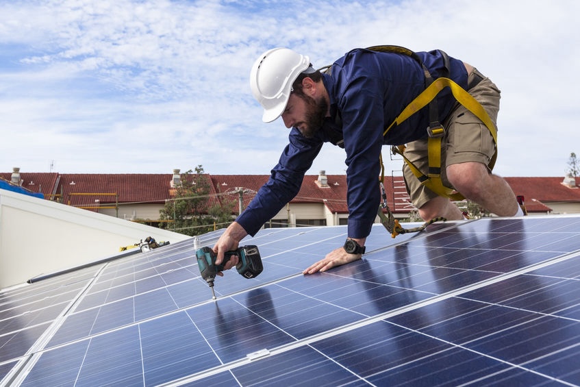 Solar panel technician with drill installing solar panels on roof